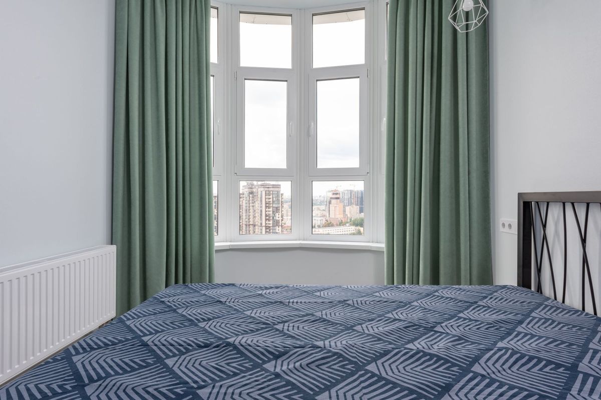 Floor-length green curtains framing a bay window in a bedroom