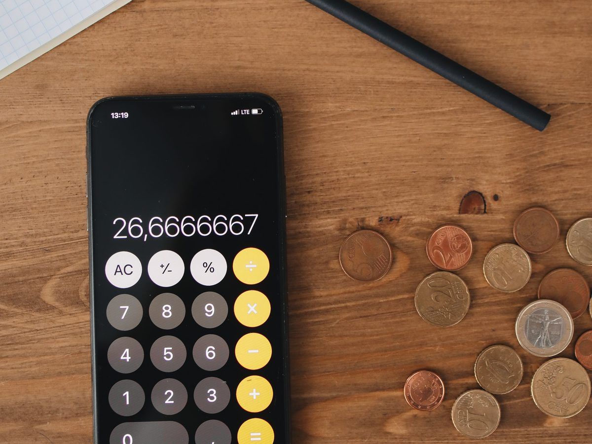 Phone calculator, coins, a notebook and a pen on a wooden table