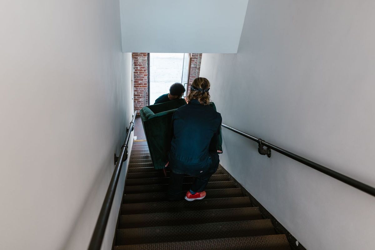 Two movers carrying a sofa down a narrow stairway
