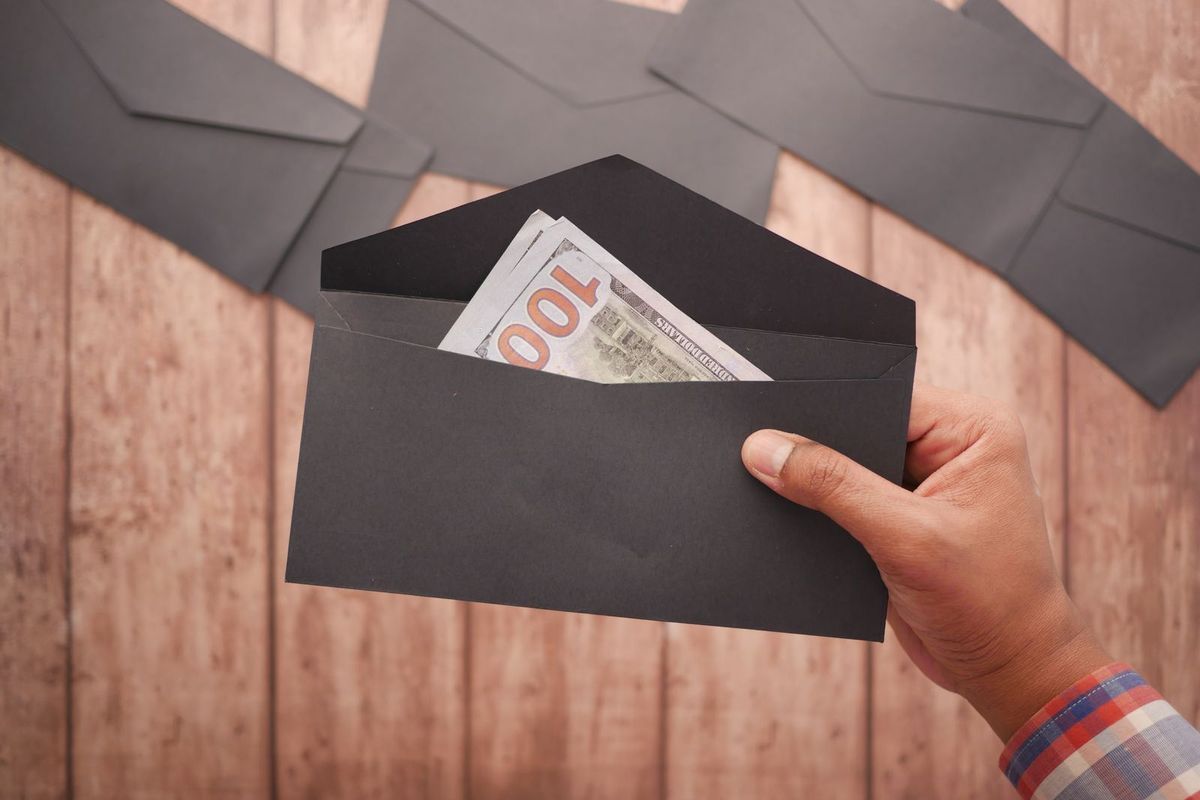 Hand holding an envelope with US dollar bills inside