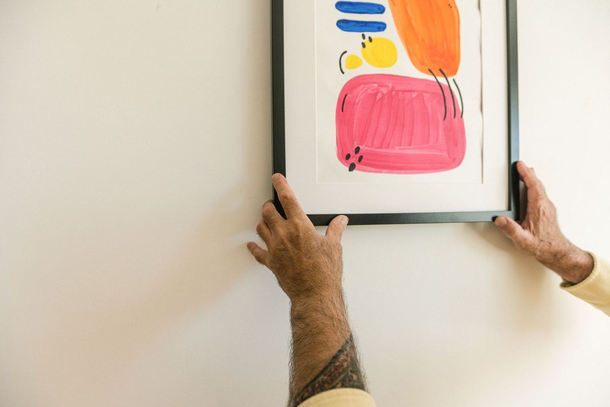 Hands pressing a framed print onto a white wall