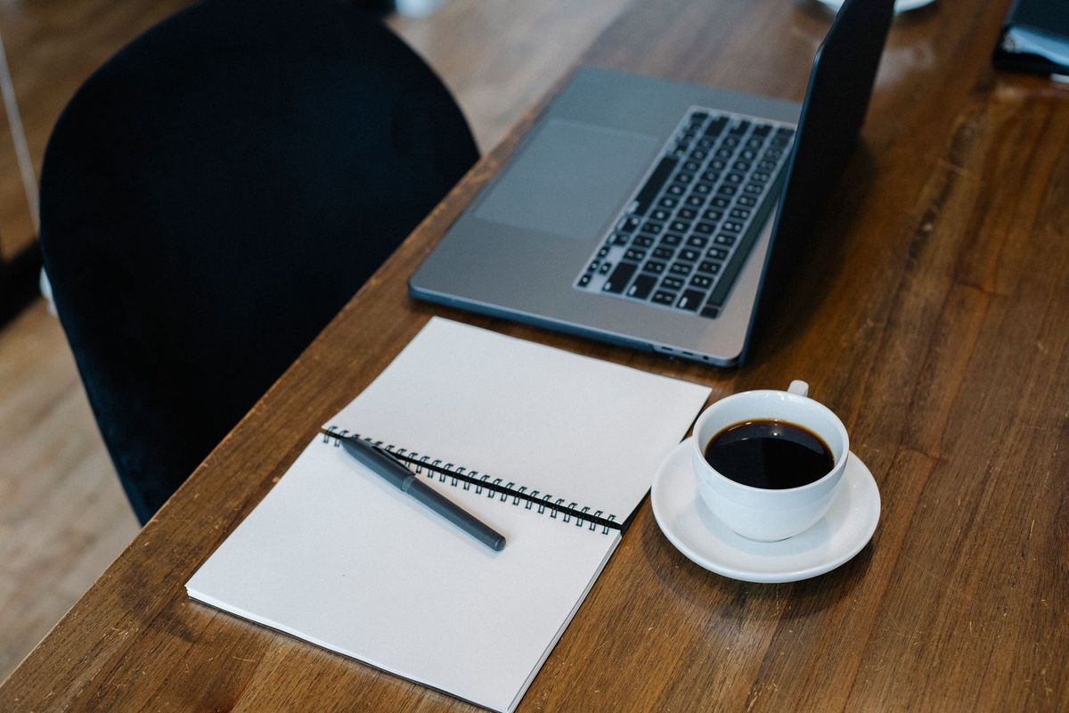 Laptop, notepad and a cup of coffee on a wooden desk