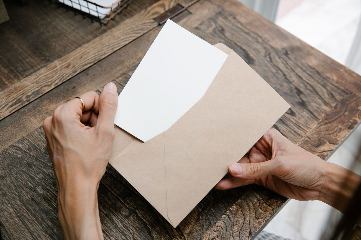 Hands pulling a letter out of an envelope on a wooden desk