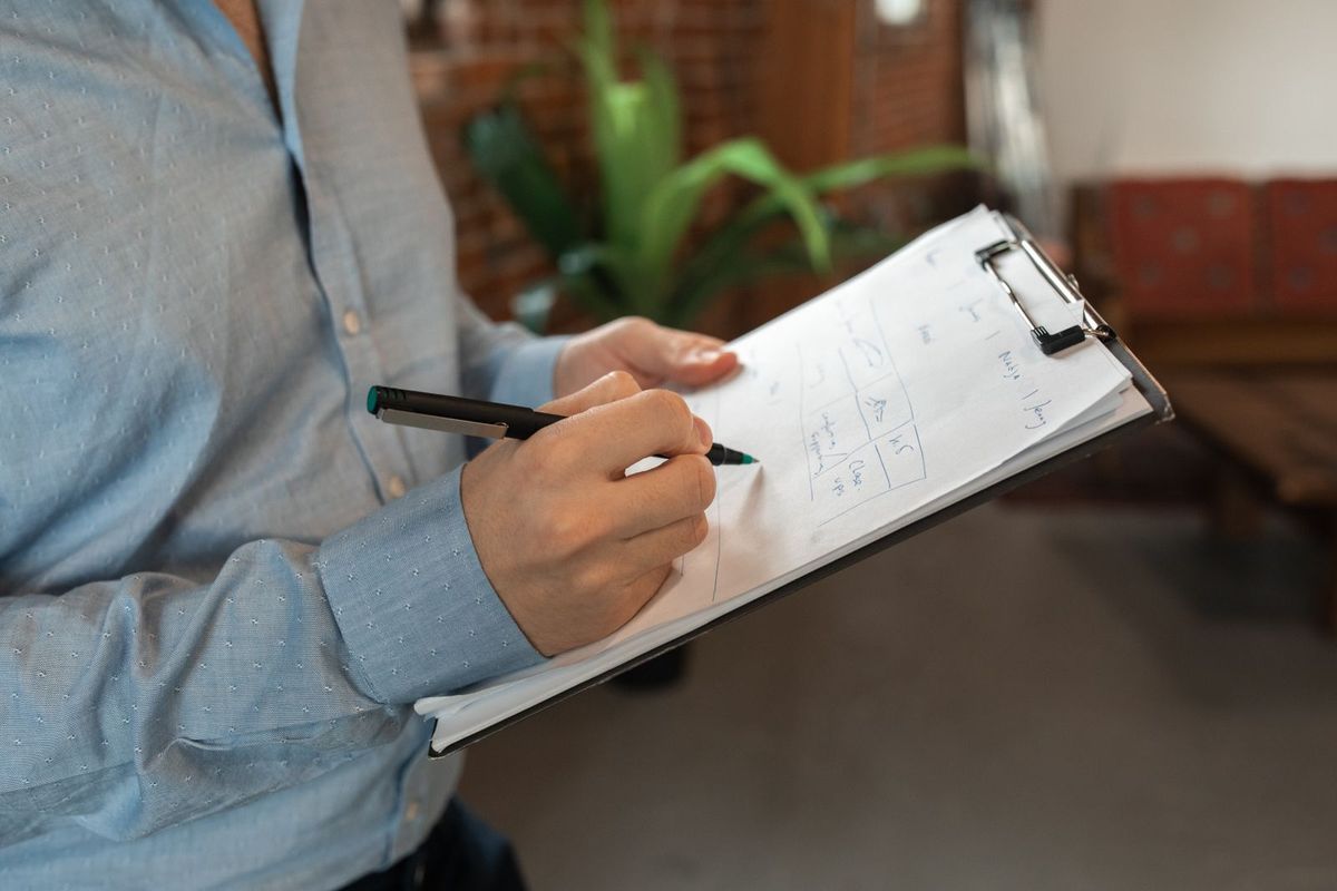 Person writing room-by-room notes on a clipboard in an apartment