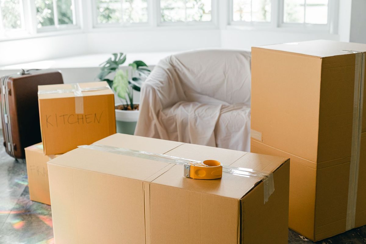 Taped moving boxes, a suitcase and a covered armchair in a bright apartment