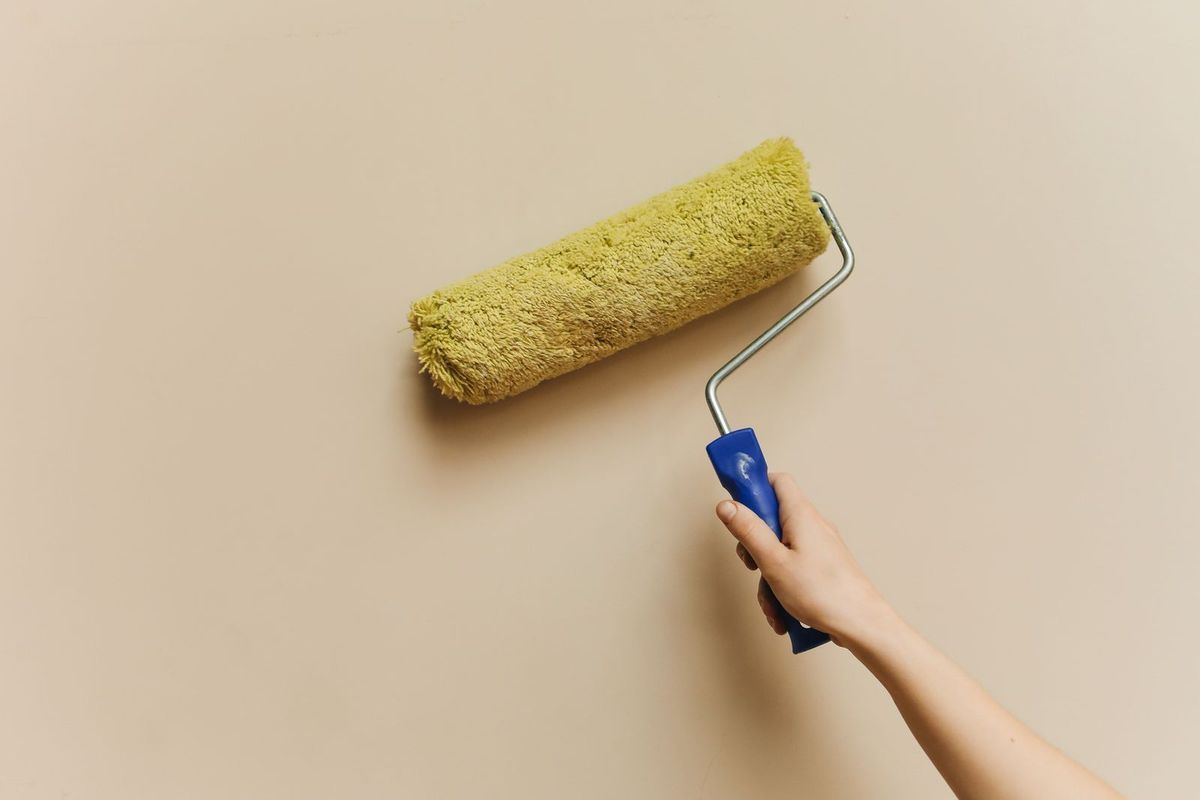 Hand holding a paint roller against a beige wall