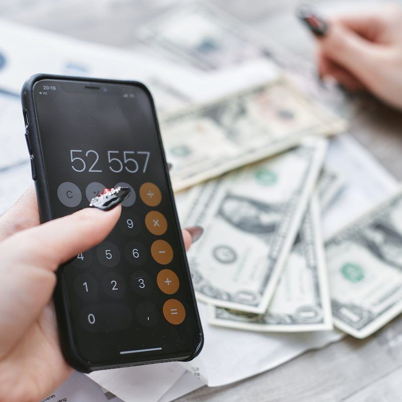 Hand using a phone calculator next to US dollar bills