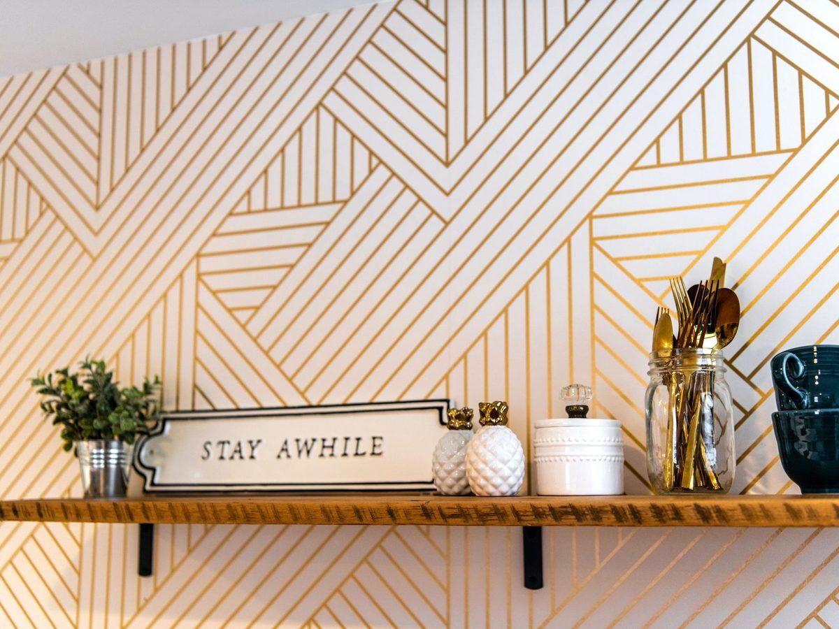 Geometric patterned wallpaper behind a shelf with small plants and a Stay Awhile sign